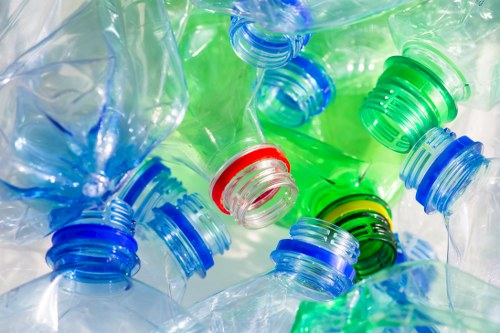 A close-up view of several used plastic bottles with different coloured caps, including blue, green, and red, piled together in a disorganized manner. The bottles are transparent with visible creases and folds, indicating they have been squeezed or crushed. The caps are tightly screwed onto the bottles, with some overlapping each other and positioned at various angles. The background is indistinct but appears to be a light, reflective surface, emphasizing the different hues and textures of the plastic waste. This collection of bottles illustrates typical household or outdoor waste that would require proper disposal or recycling services, as provided by a rubbish removal company such as Garden Clearance Archway, operating within the London area, potentially serving postal districts near N19 or NW3. The image captures the environmental aspect of waste accumulation, highlighting the importance of professional clearance to responsibly manage plastic rubbish from residential or garden contexts, compatible with outdoor waste removal services in WP postcode areas.